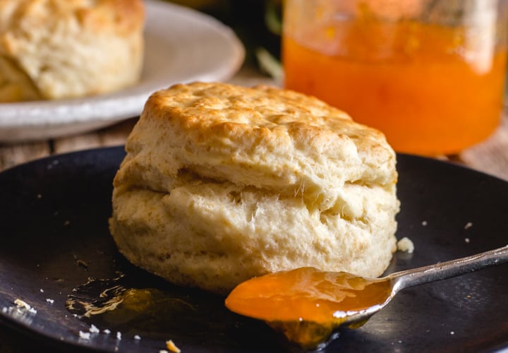 a biscuit on a black plate with a spoon of apricot jam