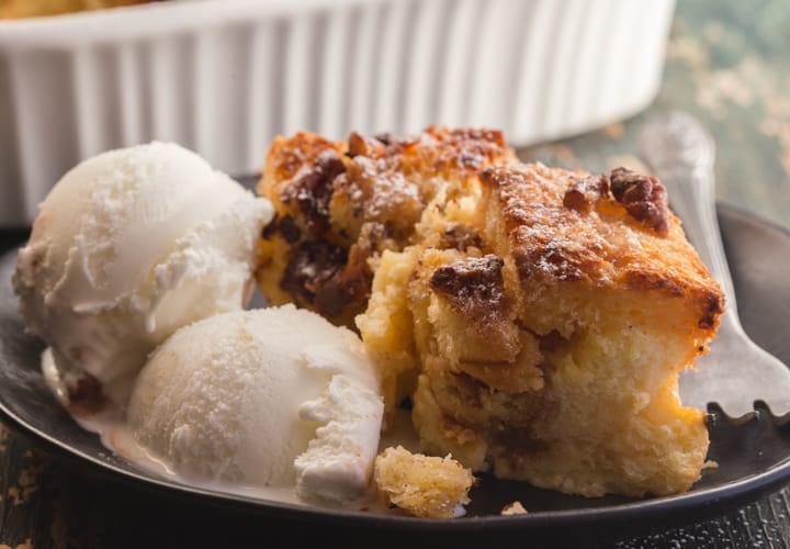 bread pudding on a black plate with 2 scoops of vanilla ice cream