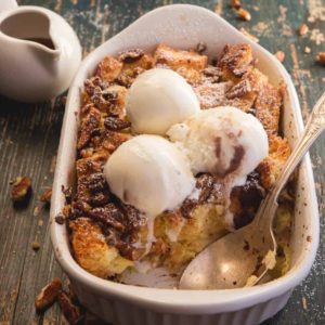 bread pudding in a white baking pan with ice cream and a spoon with a piece missing