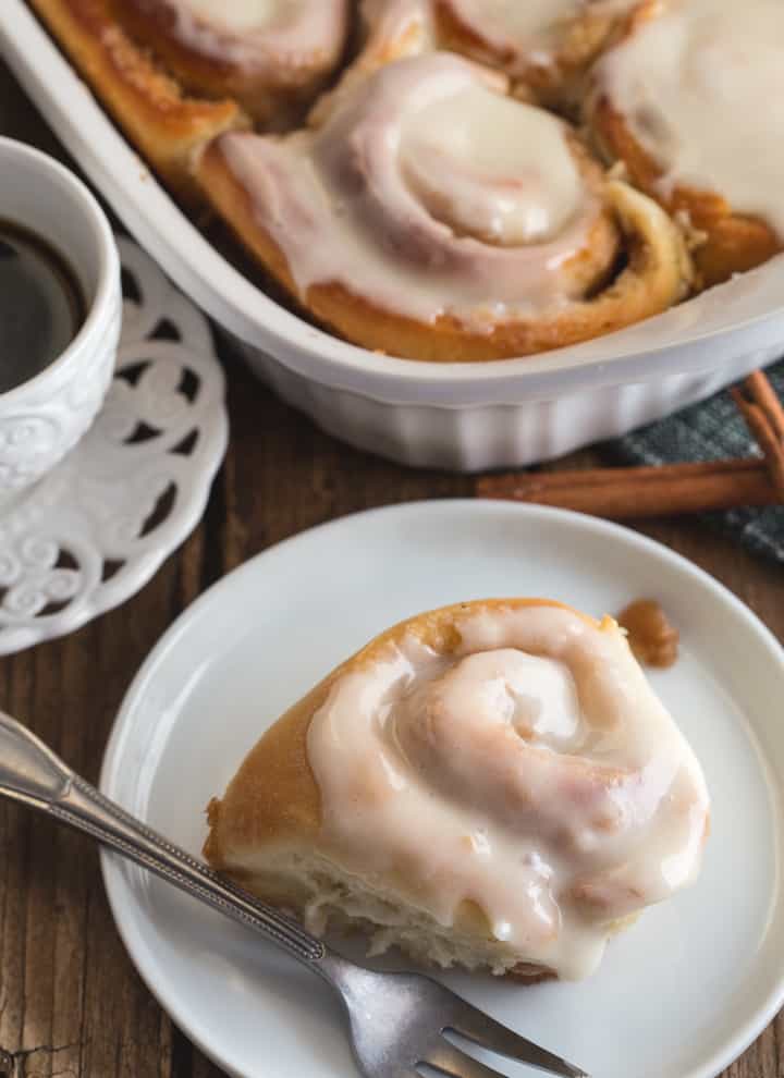 cinnamon rolls in a pan and one on a white plate with a fork