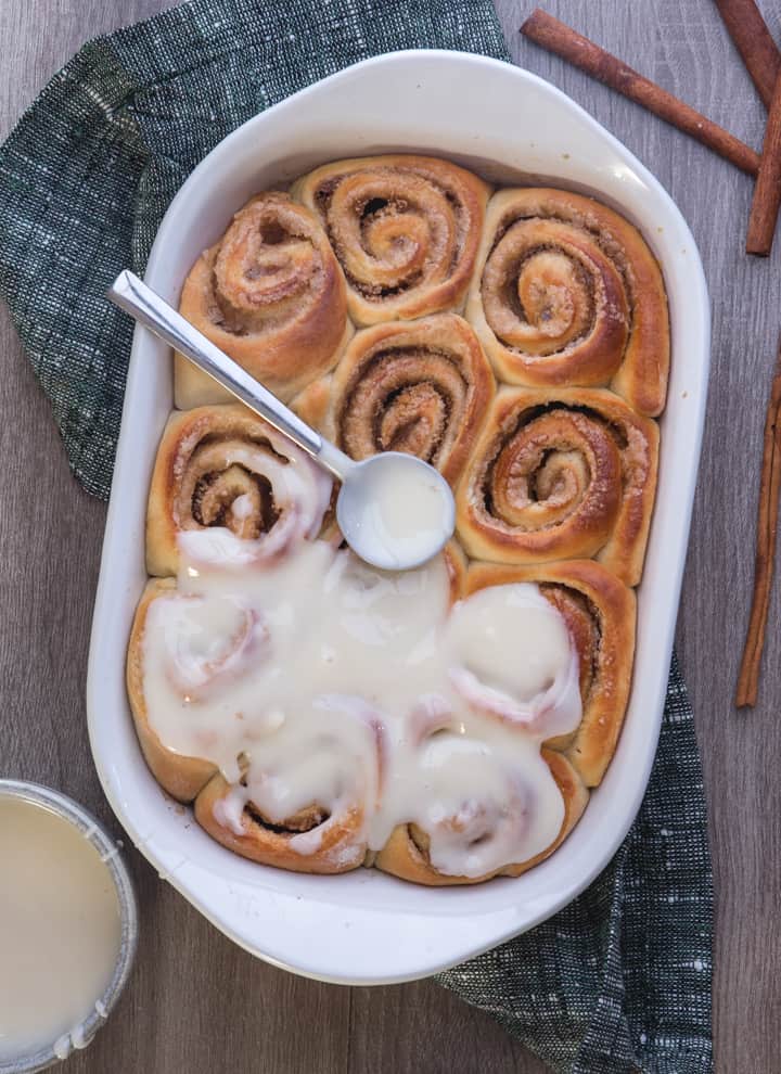 cinnamon buns in a white baking dish with glaze on top