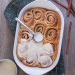 cinnamon buns in a white baking dish with glaze on top