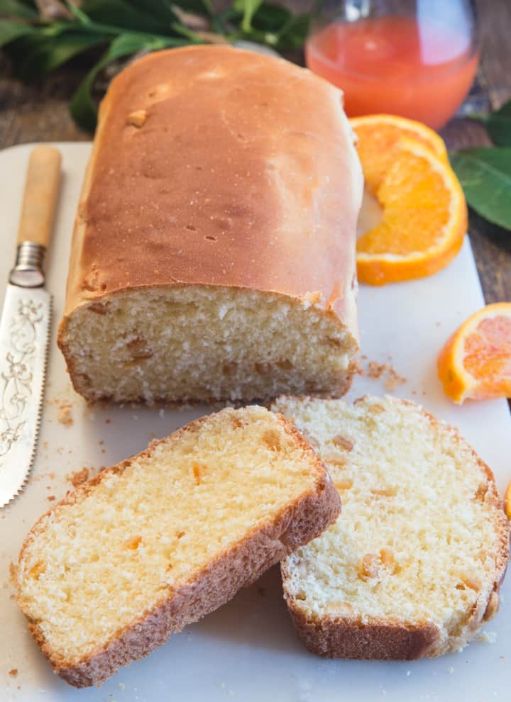 orange bread with 2 slices cut, a knife and orange slices on a white board