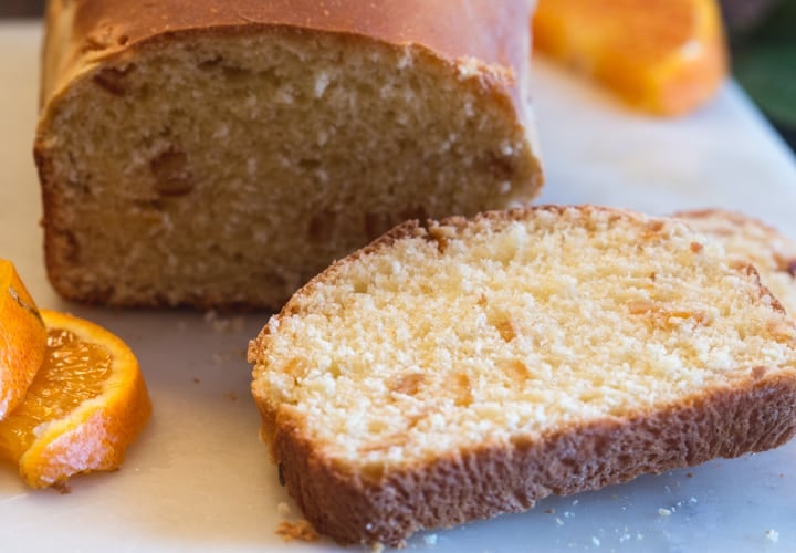 a slice of orange bread with the loaf and orange slices on a white board