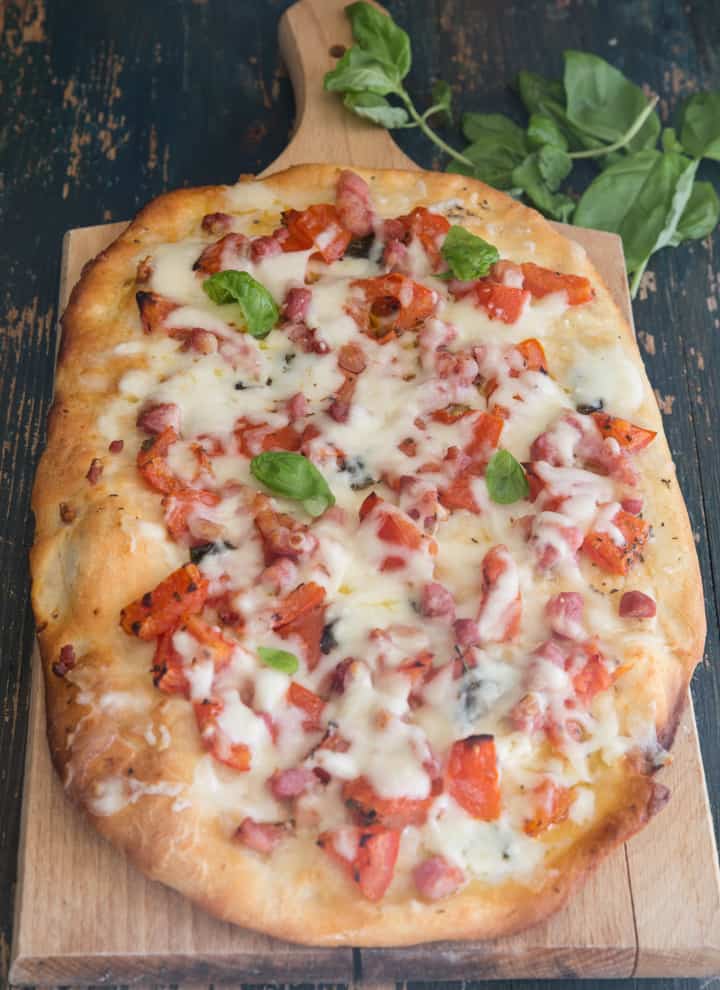 pizza with tomatoes, pancetta & cheese on a wooden board