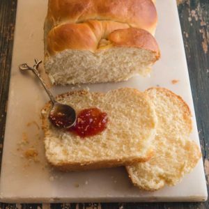yogurt brioche bread on a wooden board with 2 pieces cut with a spoon and jam
