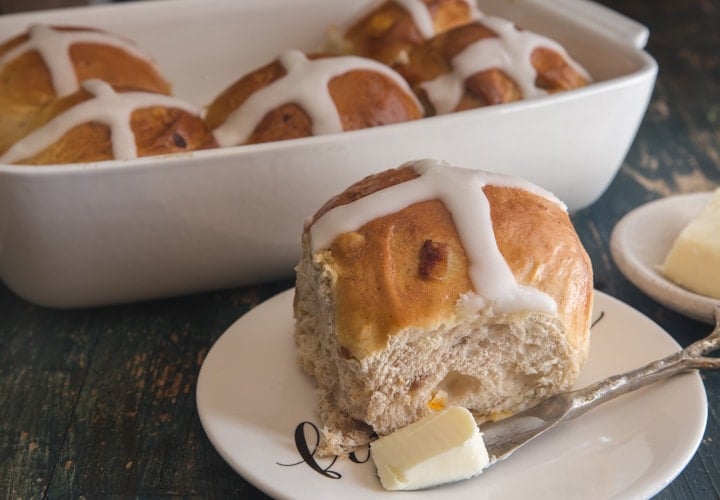 hot cross bun on a plate and the rest in a white baking dish