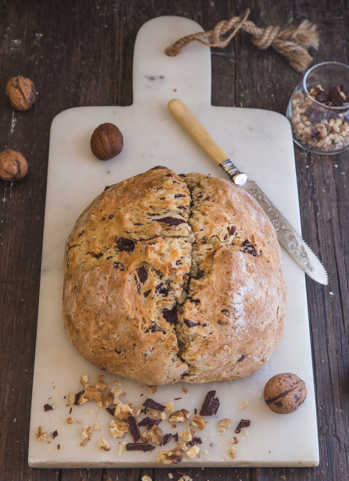 irish soda bread baked on a white board with a knife and nuts