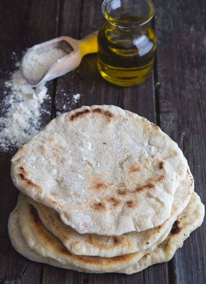 4 flatbreads on top of each other with flour and oil in the back ground