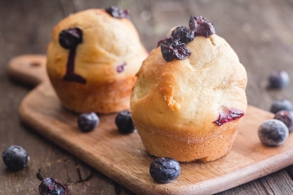 2 muffins on a wooden board with blueberries scattered