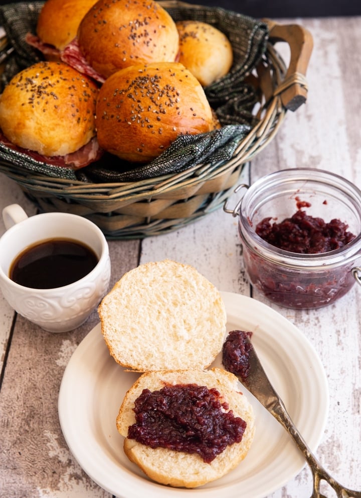 buns in a basket and one on a white plate with jam
