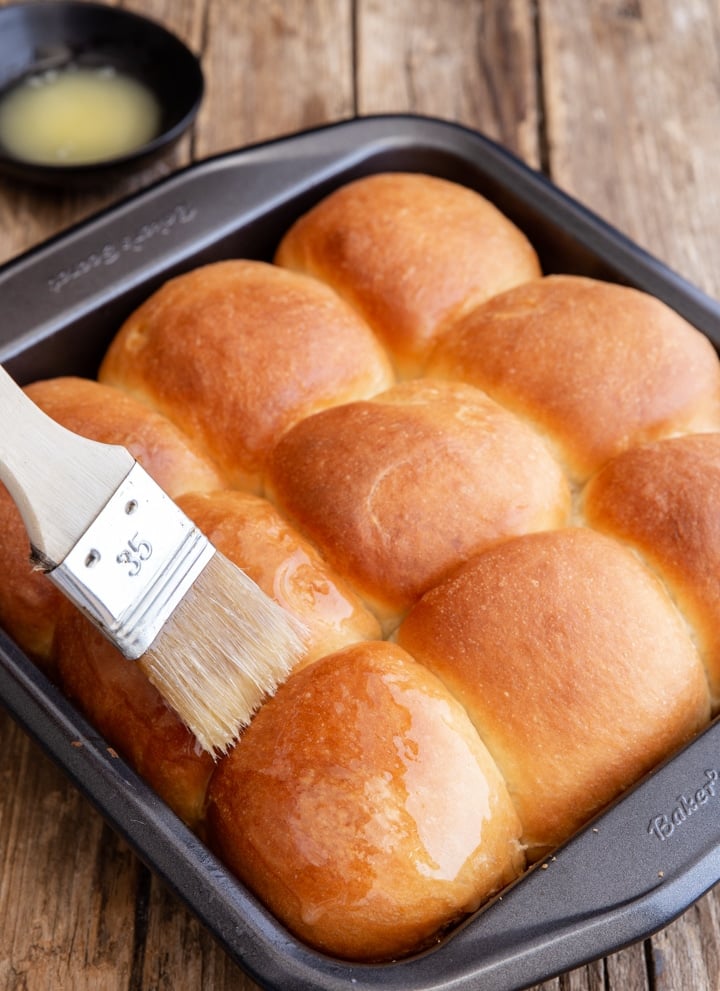 brushing melted butter on dinner rolls in the baking pan