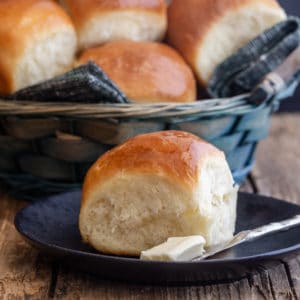 dinner rolls in a basket and one on a black plate with a knife and butter