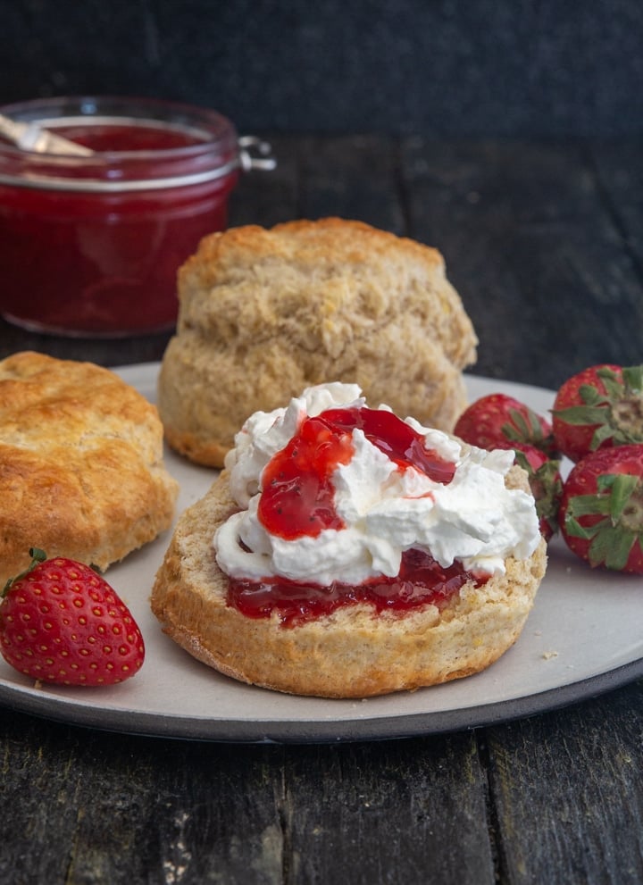 scones on a white plate with jam and whipped cream.