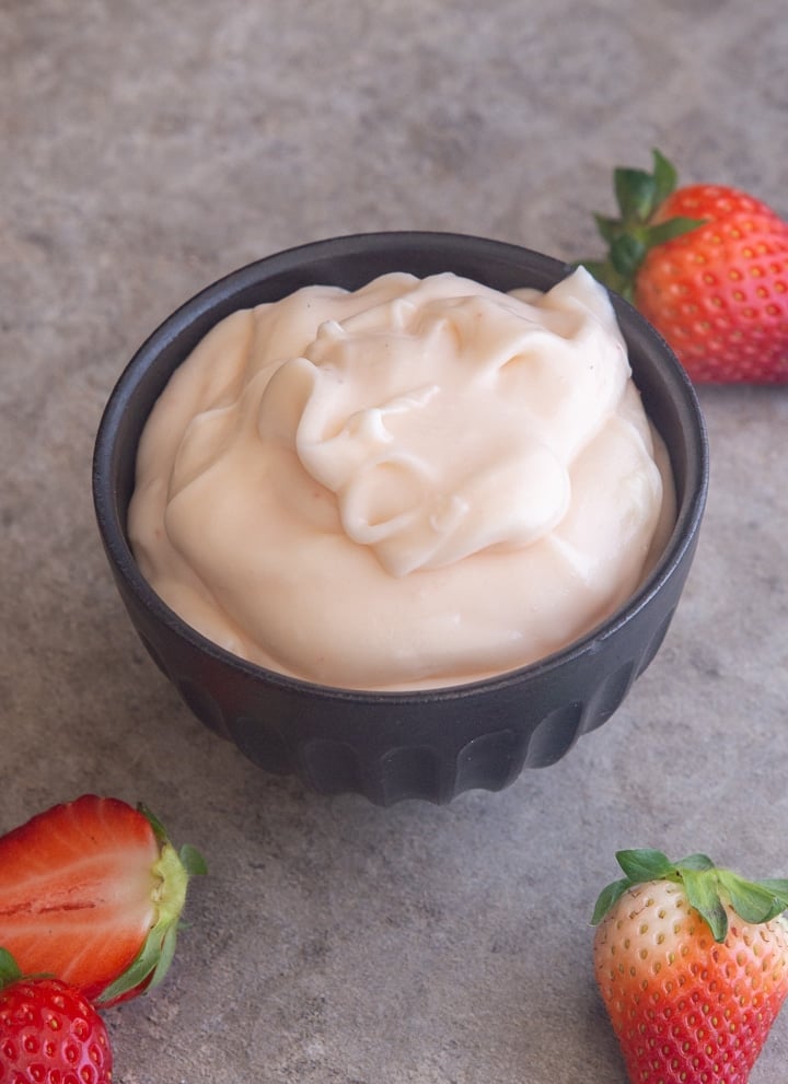 frosting in a black bowl with strawberries around the bowl.