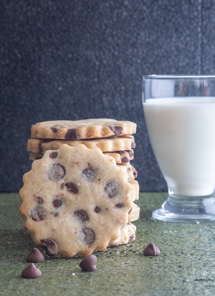 Cookies stacked with one leaning again them and a glass of milk.