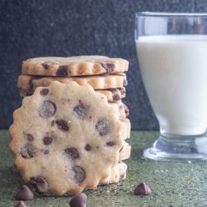 Cookies stacked with one leaning again them and a glass of milk.