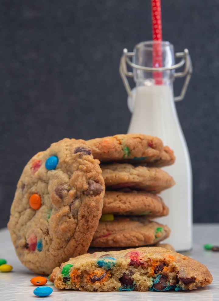 Cookies stacked and one leaning, with one cut in half & a small bottle of milk with a red straw in it.