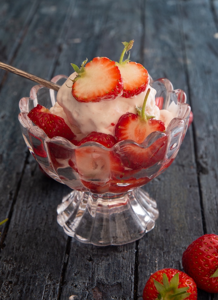 Strawberry ice cream with strawberries in a glass dish.