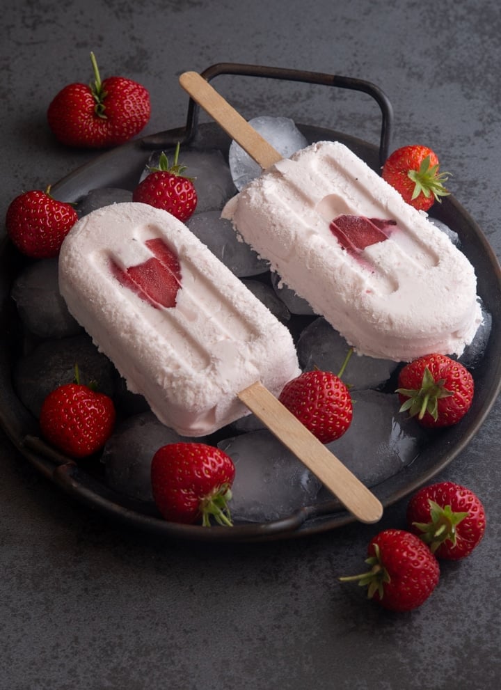 2 strawberry ice cream popsicles on a a place plate with strawberries.