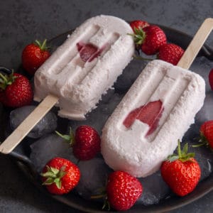 2 strawberry ice cream popsicles on a a place plate with strawberries.