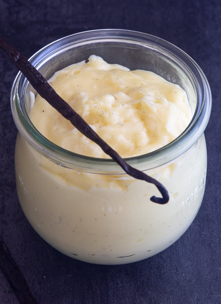 Vanilla pastry cream in a glass jar with a vanilla bean across the top.