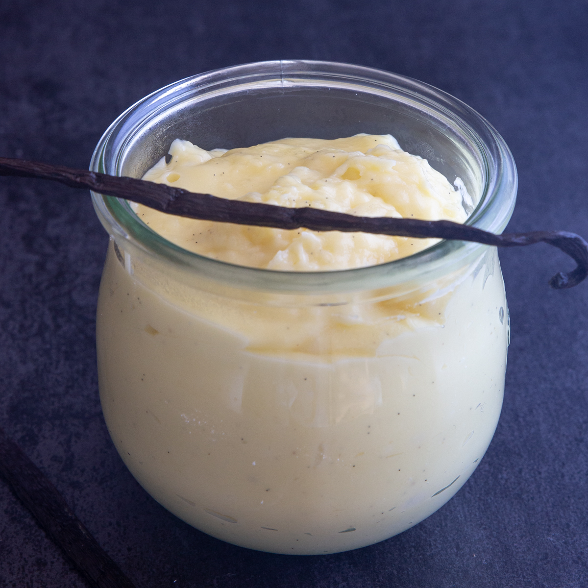 Vanilla pastry cream in a glass jar with a vanilla bean across the top.