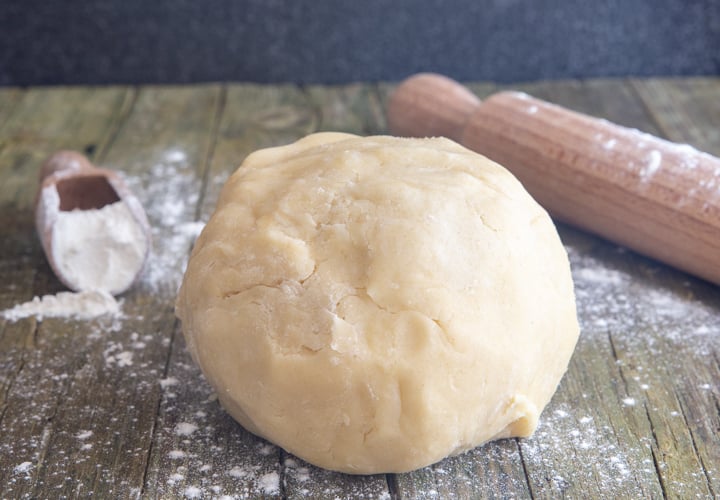 Pie Dough on a wooden board with flour in a scoop and a rolling pin.
