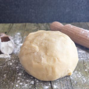 Pie Dough on a wooden board with flour in a scoop and a rolling pin.