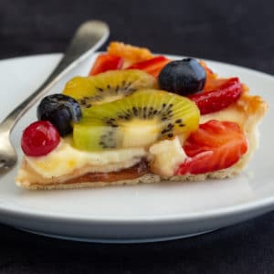 A slice of fruit flan on a white plate with a fork.
