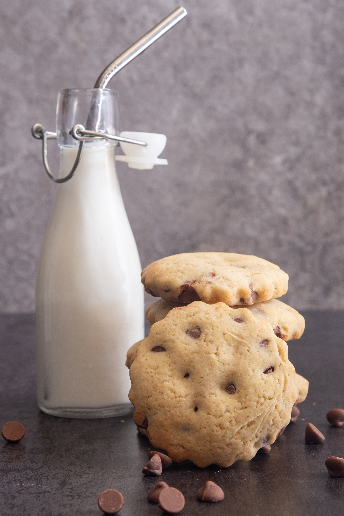 Cookies stacked with one leaning and a small bottle of milk with a silver straw.
