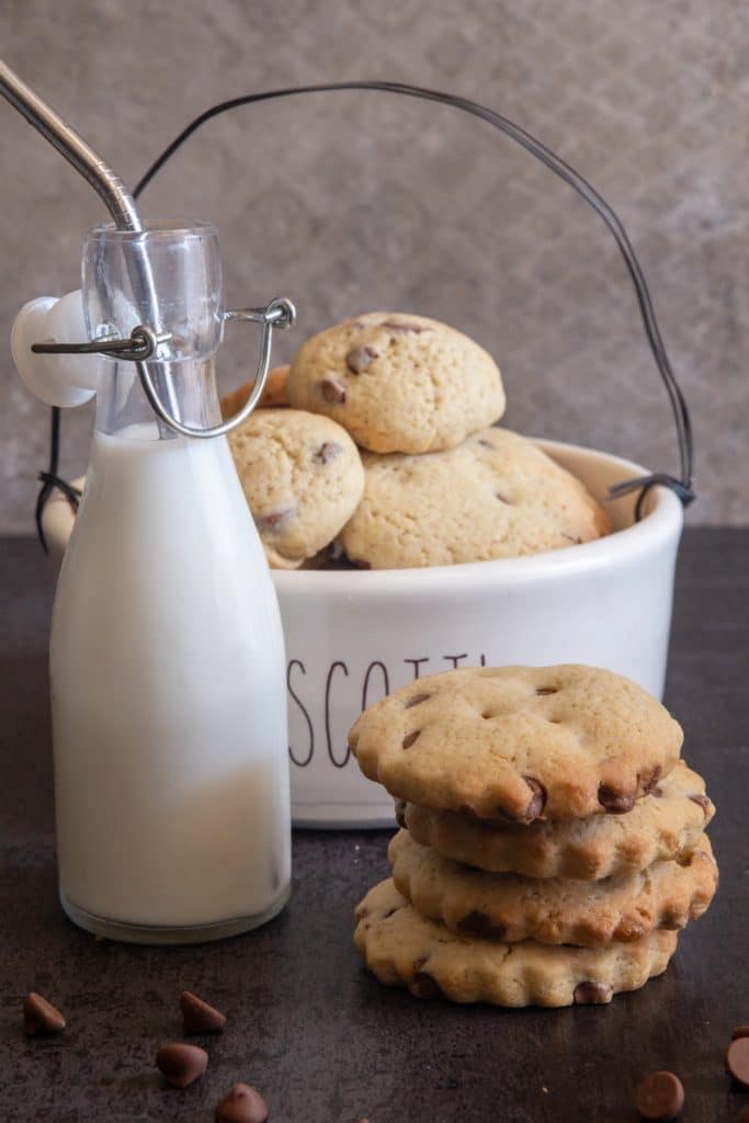 Cookies stacked and cookies in the bowl and a bottle of milk with a silver straw.