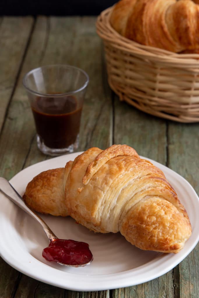 Croissant in a basket with one on a plate with jam.