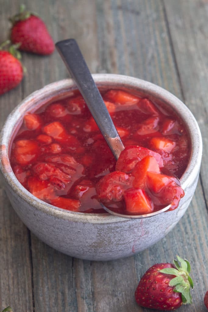 Strawberry sauce in a white bowl with some on a spoon.