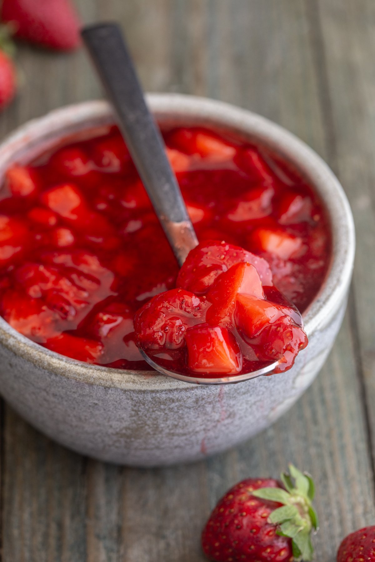 Strawberry sauce in a white bowl with some on a spoon.