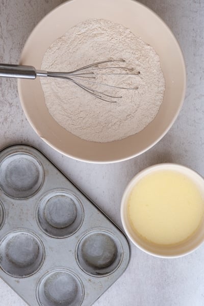 Whisked dry ingredients in a white bowl and wet ingredients in a small bowl, with a 6 muffin tin.