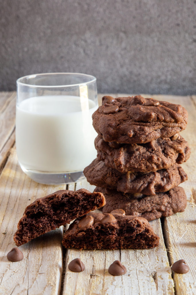Cookies stacked with one cut in half and a glass of milk.