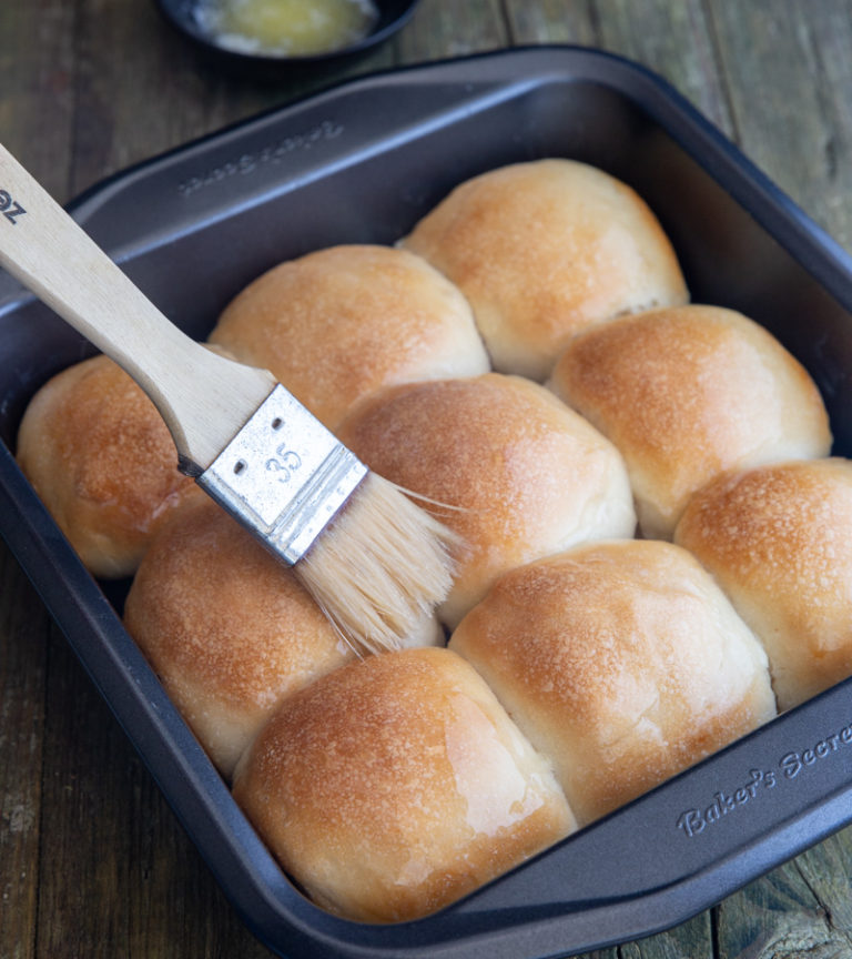 Sourdough dinner rolls in a black pan brushed with butter.