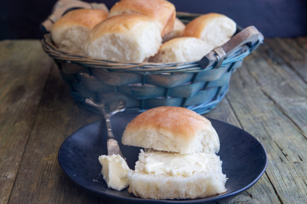 Dinner rolls in a basket and one cut in half with butter.