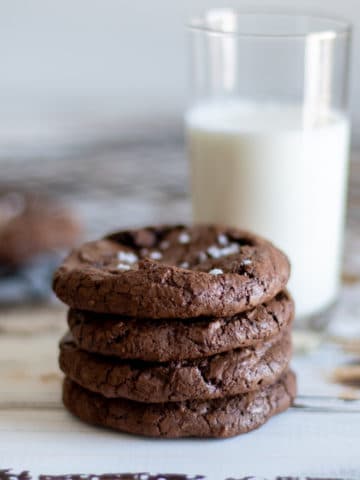 4 brownie cookies stacked with a glass of milk.