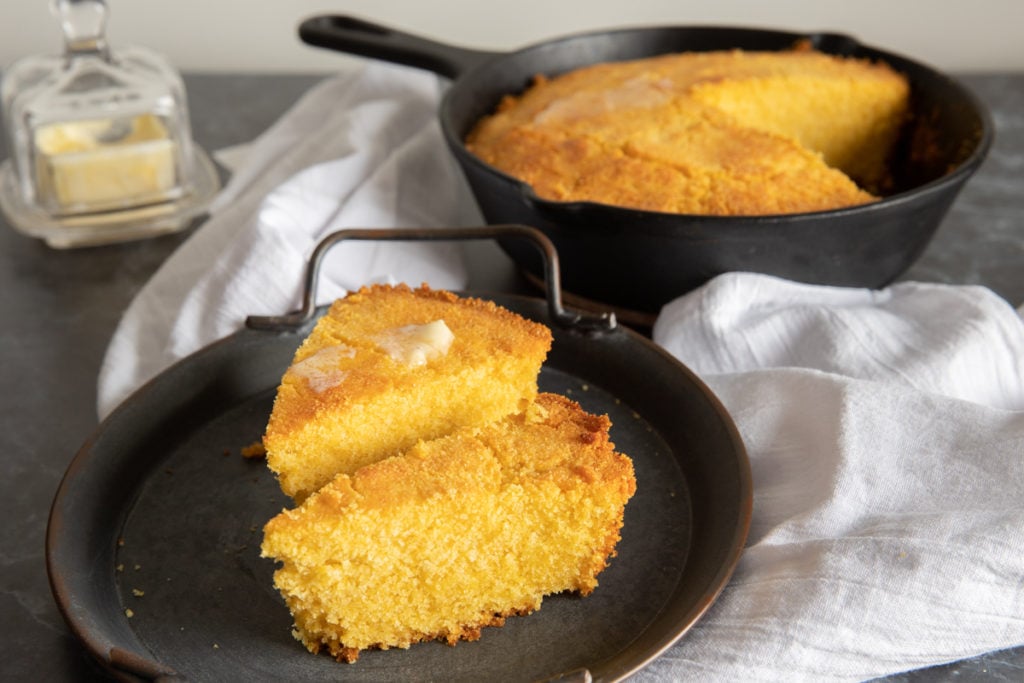 corn bread in a pan and 2 slices on a black plate.