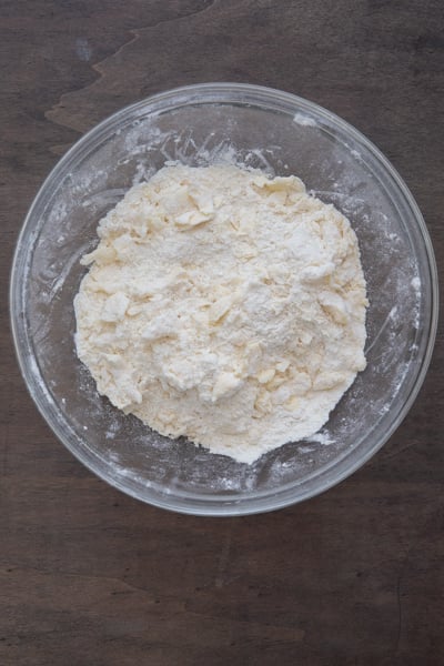 Mixing the butter with dry ingredients to form coarse crumbs in a glass bowl.