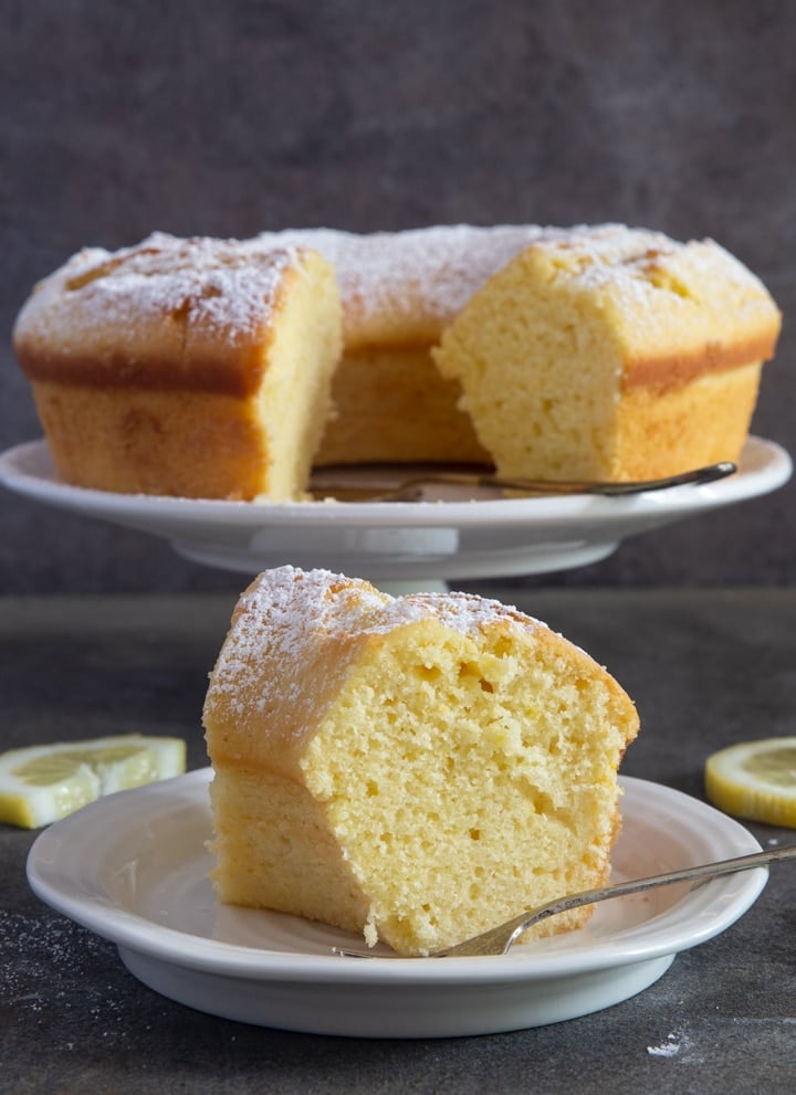 Lemon bundt cake on a cake stand with a slice on a white plate.