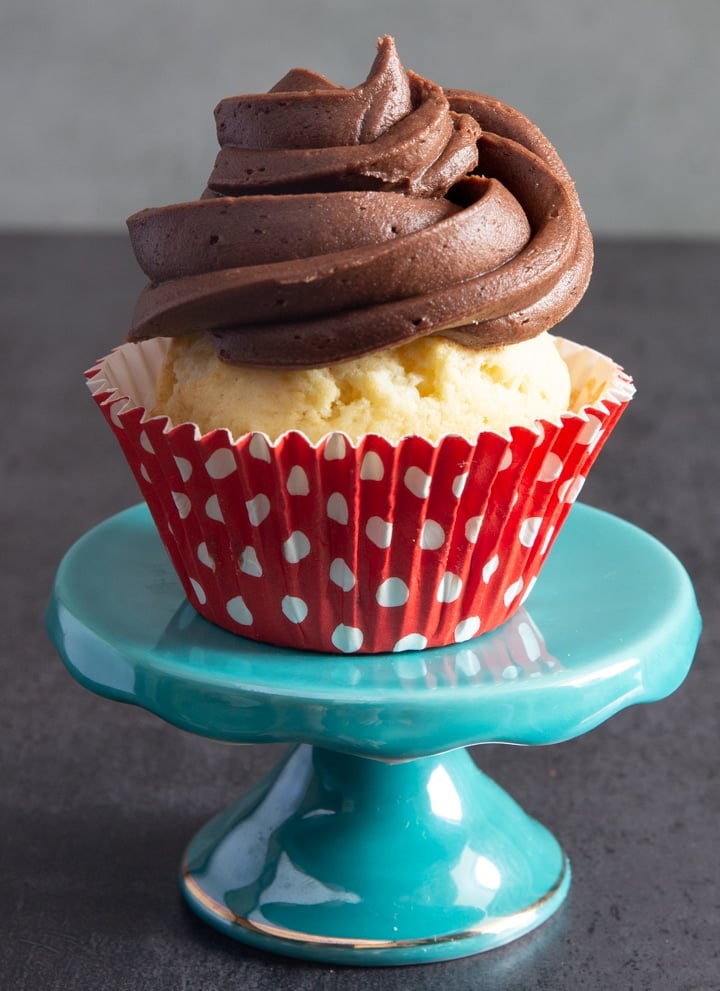 Vanilla cup cake on blue stand with chocolate frosting.