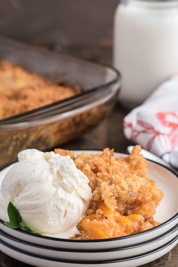 Peach crumble in a baking dish and some on a plate with a scoop of ice cream.