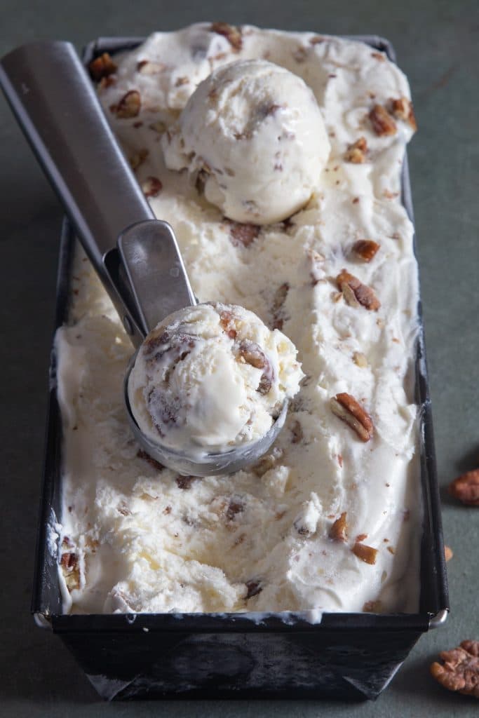 Pecan ice cream in a loaf pan with a scoop.