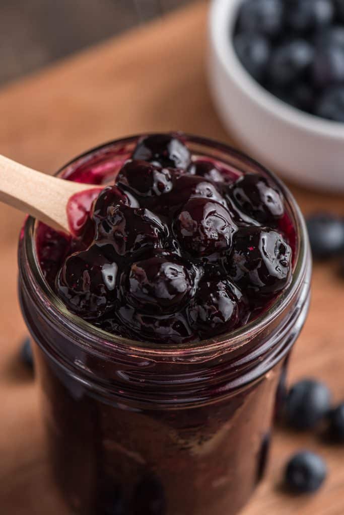 The berry sauce in a glass jar with a wooden spoon.
