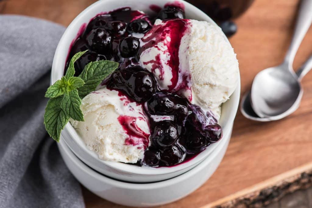 blueberry sauce on ice cream in a white bowl.