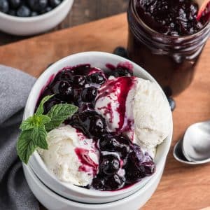 Blueberry sauce on vanilla ice cream in a white bowl.