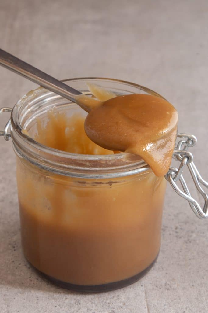 Spoonful of caramel sauce on top of a glass jar.